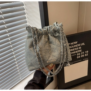 Detail of light blue denim bucket bag with quilted texture and silver chain strap