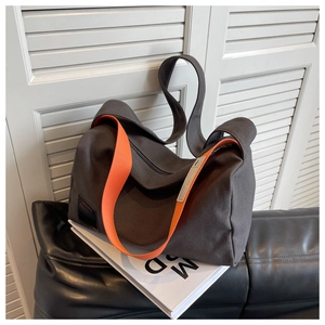 Detail showing charcoal canvas crossbody bag with vibrant orange wide strap and side patch