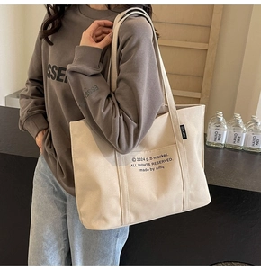 Detail of cream canvas tote bag with front pocket and minimalist letter print strap