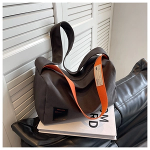 Detailed view of the dark grey canvas bag with bold orange strap and brand patch
