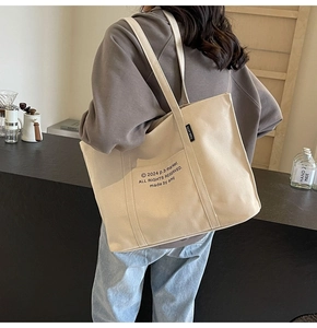 Detailed shoulder view of a large cream canvas tote bag with black letter printing
