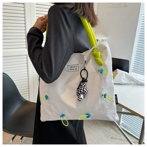 Detail of white tote bag featuring neon green handles and black checkered knot charm