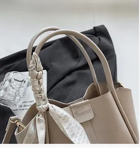 Detail of beige bucket bag handle with decorative geometric silk scarf and brand logo