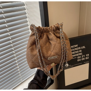 Close-up of brown quilted bucket bag with silver chain strap and metal pendant detail