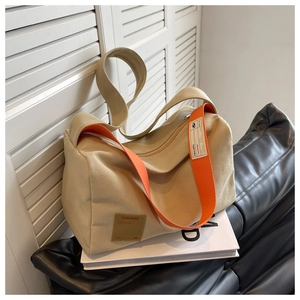 Detail of khaki canvas crossbody bag with orange wide strap and brown leather brand tag