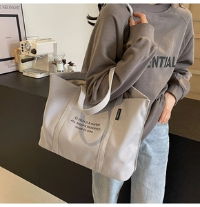 Detail of grey canvas tote bag with letter print and side label for daily commuting