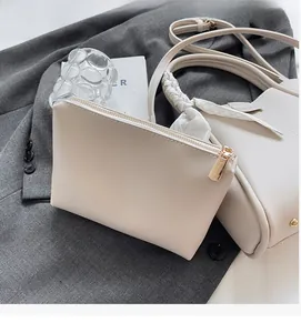 Close-up of a cream-colored leather mini pouch with a golden zipper on a grey blazer