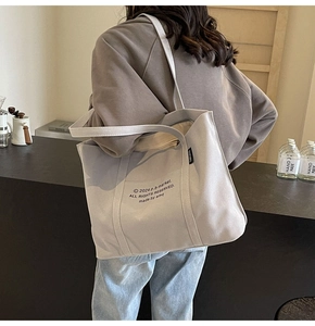 Detail of light grey canvas tote bag with black lettering and durable shoulder straps