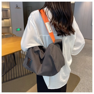 Detail of grey canvas crossbody bag with contrast orange wide strap on female model