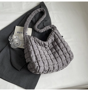 Close-up of grey quilted puff tote bag with ruched shoulder strap on white bedding