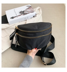 Detail of black nylon crescent fanny pack with gold zippers and white FASHION letter strap