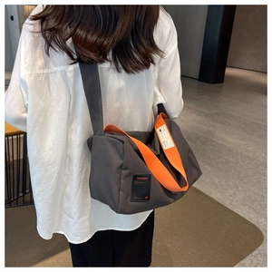 Detail of grey canvas crossbody bag with orange straps on female model back view