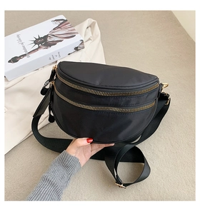 Detail of a black nylon crescent waist bag with dual golden zippers and wide strap