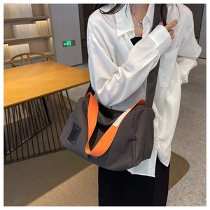 Large gray canvas crossbody bag with vibrant orange wide strap and black logo patch