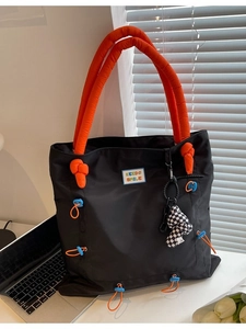 Chic black nylon tote bag with orange padded handles and checkerboard mushroom charm
