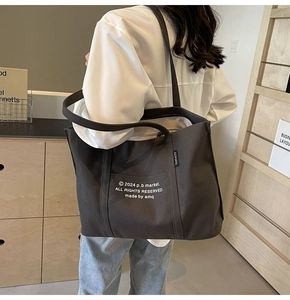 Detail of dark brown canvas tote bag featuring white letter print and side brand label