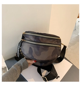 Detail of camouflage crossbody bag featuring double gold zippers and a wide shoulder strap