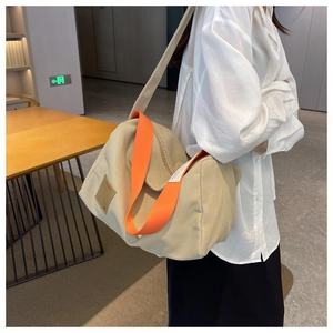 Detail view of large canvas crossbody bag with wide orange strap and beige fabric texture