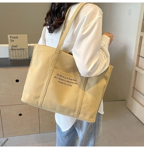 Detail of khaki canvas tote bag with black letter print on a shoulder-carried strap