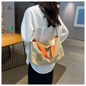 Detail of beige canvas crossbody bag featuring a vibrant orange wide shoulder strap