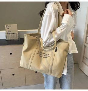 Detail of canvas tote bag showing dual straps, front pocket and letter print details