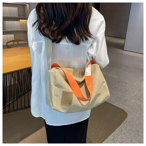 Detail view of large beige canvas crossbody bag with bright orange wide shoulder strap