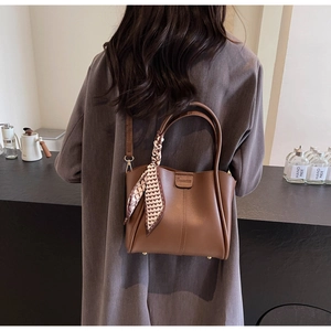 Brown leather bucket bag with heart print scarf handle detail shown on a female model