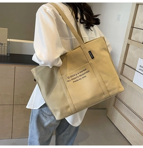 Detail shot of the khaki canvas tote bag showing the front pocket and logo patch