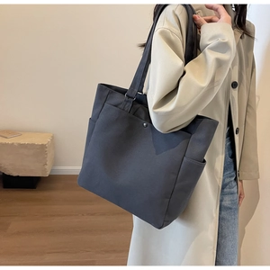 Detail view of dark grey canvas tote bag showing the front pocket and metal rivet detail