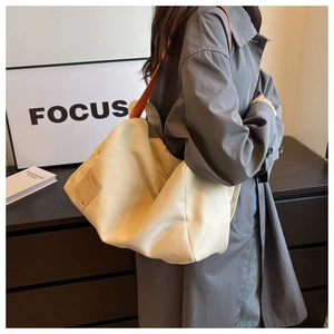 Detail of minimalist canvas tote with orange strap and woven label on a model