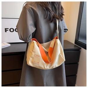Detail of canvas crossbody bag with vibrant orange strap and brand woven label