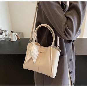 Detail of cream bucket bag with decorative scarf and logo in a commuter setting
