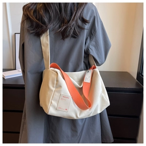 Detail of canvas pillow bag with vibrant orange wide strap and brand logo patch