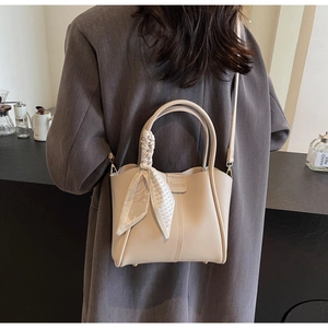 Detail of beige structured handbag with silk scarf handle, paired with a stylish grey blazer