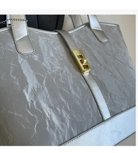 Detailed macro view of silver tote bag featuring pleated texture and golden square twist lock