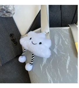 Close-up of white plush cloud charm with striped ropes on a silver shoulder bag