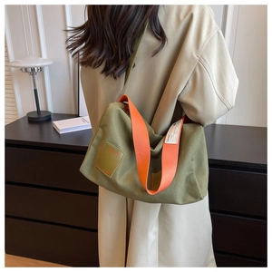 Detail of green canvas crossbody bag with orange strap and woven label decoration