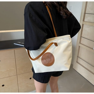 Detalle del bolso tote de lona con asas de cuero marrón y parche de logo circular