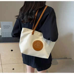 Detalle de bolso tote de lona blanca con asa de cuero marrón y parche de logo circular