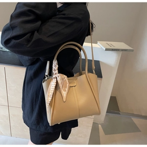 Modern khaki bucket bag shown with silk scarf detail and crossbody strap on a model