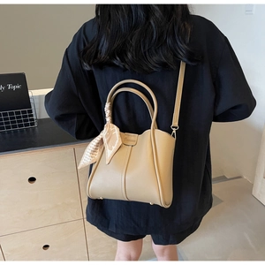 Detail of khaki bucket bag with decorative silk scarf on handle worn by a model