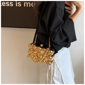 Macro detail of gold sphere acrylic clutch bag showing metal texture and chain strap