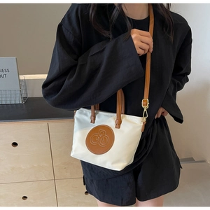 Detalle del bolso tote de nailon crema con asas de cuero marrón y parche de logotipo redondo