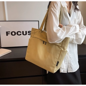 Detail of a yellow canvas tote bag showing front zipper pocket and side open compartment