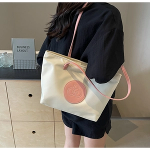 Primer plano de un bolso tote crema con asas rosas llevado por una modelo de moda