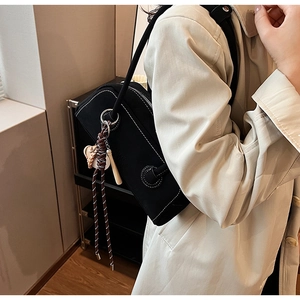 Detail of black canvas bag with white contrast stitching and wooden bead charm on shoulder