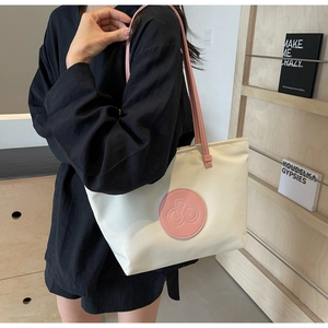 Detalle del bolso tote crema con asas rosas y parche de logo circular sobre el hombro