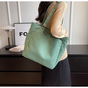 Detail of sage green canvas tote bag showing side pocket and durable strap on a model