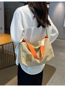 Minimalist beige canvas crossbody bag with orange strap shown in a back view on a model