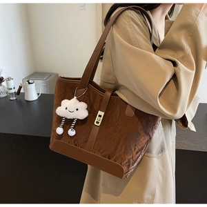 Close-up of brown textured tote bag with gold lock and cloud charm on model's shoulder